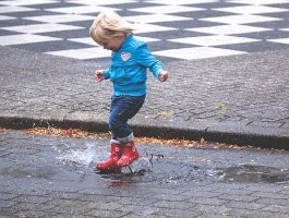 Kind springt mit rote Gummistiefeln in Pfütze