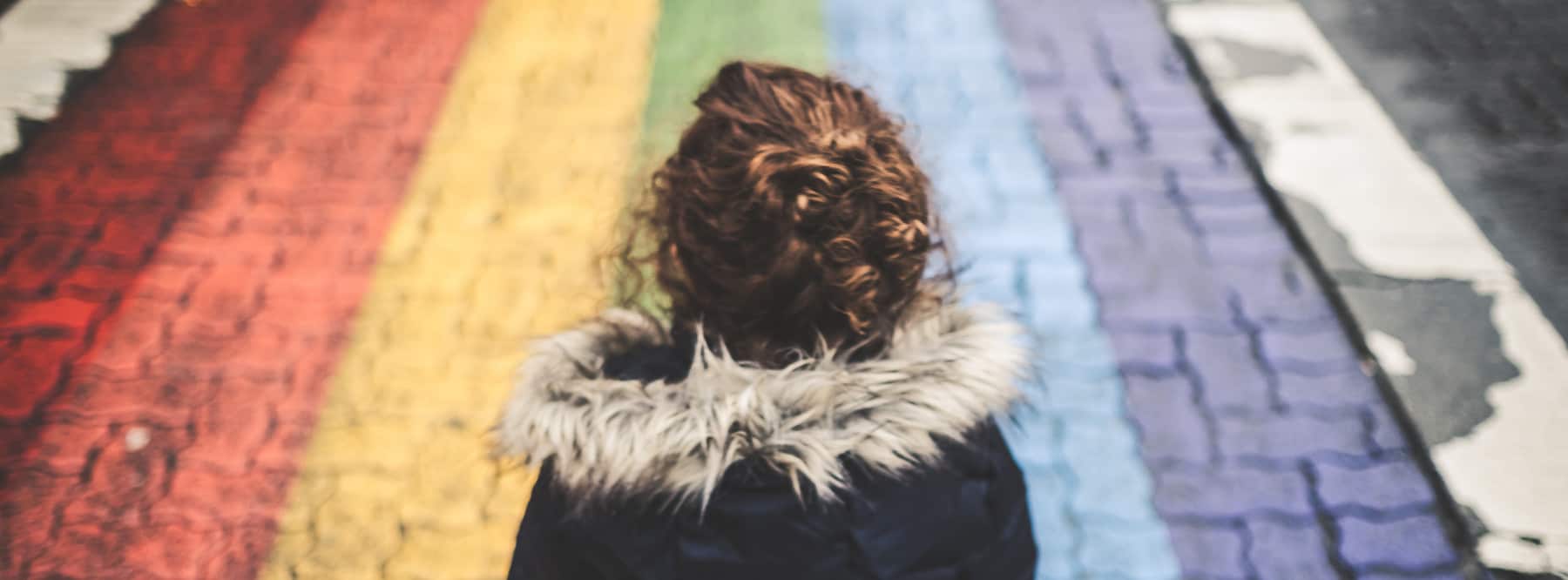Eine Frau steht vor einem mit einem Regenbogen bemalten Stück Asphalt.