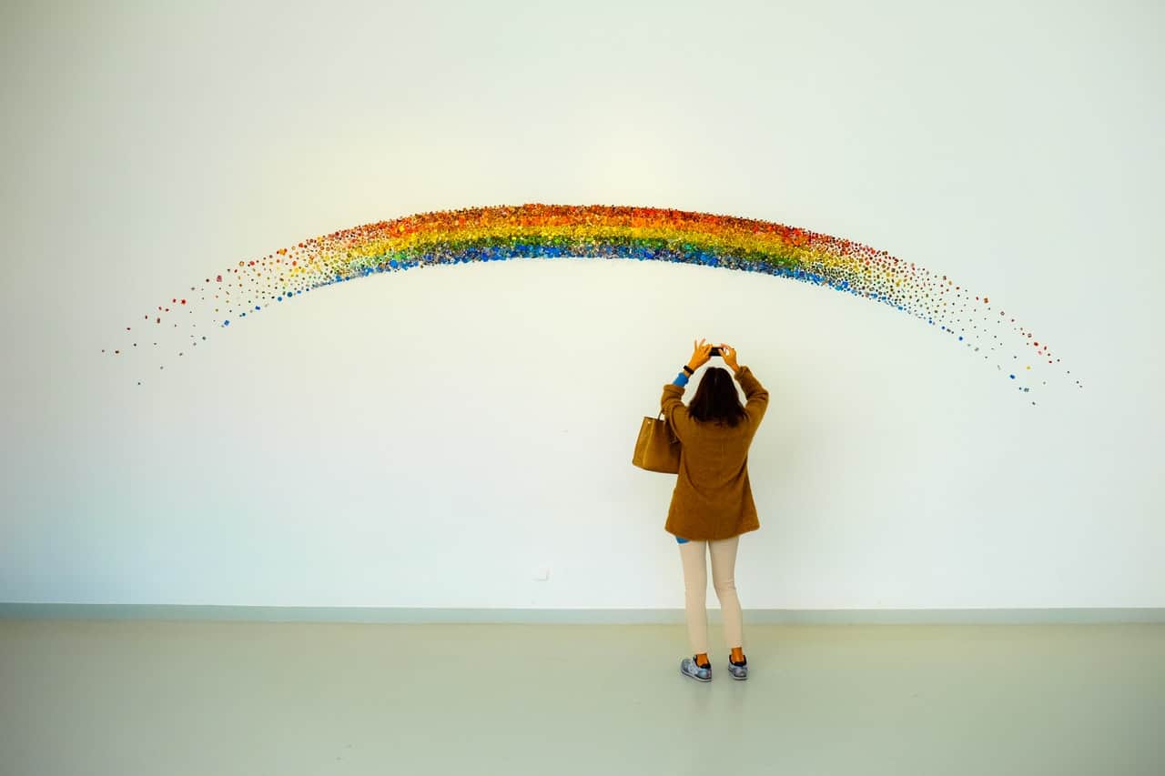 Eine Frau steht vor einem Kunstwerk mit einem Regenbogen.